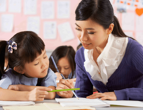 A teacher helping a little girl with her homework in a classroom